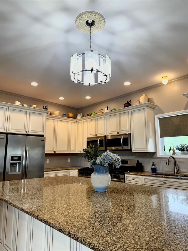 kitchen with appliances with stainless steel finishes, sink, pendant lighting, dark stone countertops, and white cabinetry