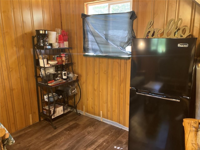 kitchen with black refrigerator, dark hardwood / wood-style floors, and wood walls