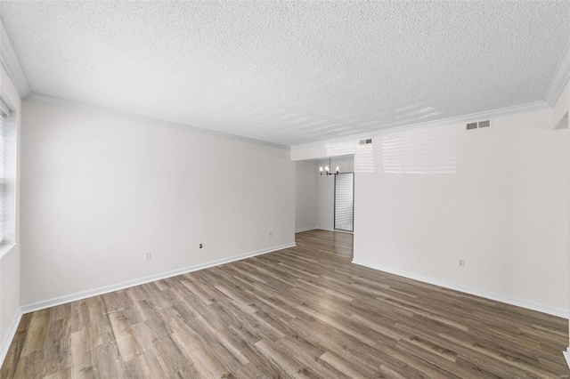 spare room with a textured ceiling, hardwood / wood-style flooring, crown molding, and a notable chandelier