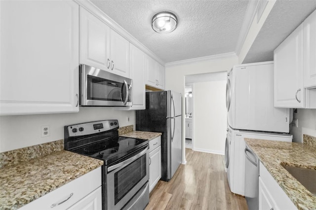 kitchen with appliances with stainless steel finishes, a textured ceiling, crown molding, stacked washer and dryer, and white cabinetry