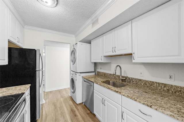 kitchen with sink, stainless steel appliances, a textured ceiling, white cabinets, and stacked washer and clothes dryer