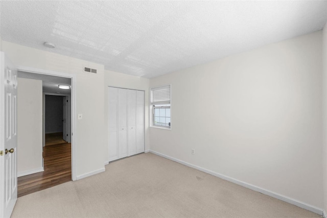 unfurnished bedroom with a closet, light colored carpet, and a textured ceiling