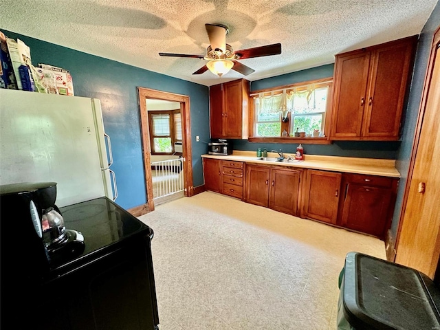 kitchen featuring a healthy amount of sunlight, black electric range oven, white fridge, and a textured ceiling