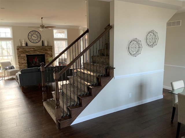 stairs featuring hardwood / wood-style flooring, ceiling fan, a healthy amount of sunlight, and a stone fireplace