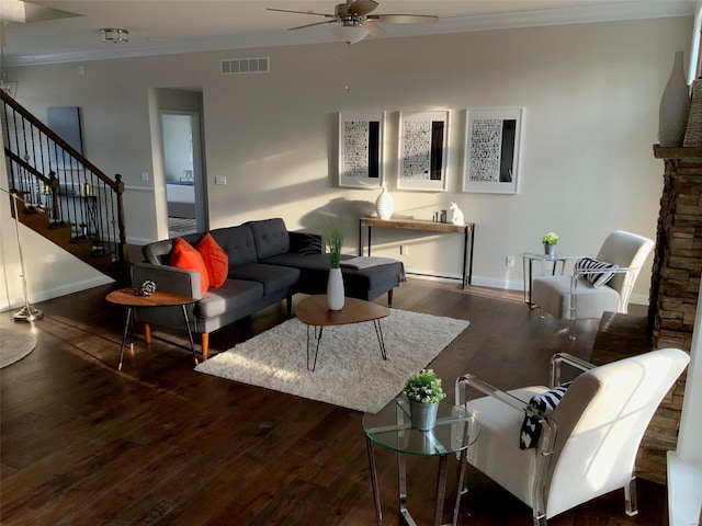 living room with crown molding, ceiling fan, dark wood-type flooring, and a stone fireplace