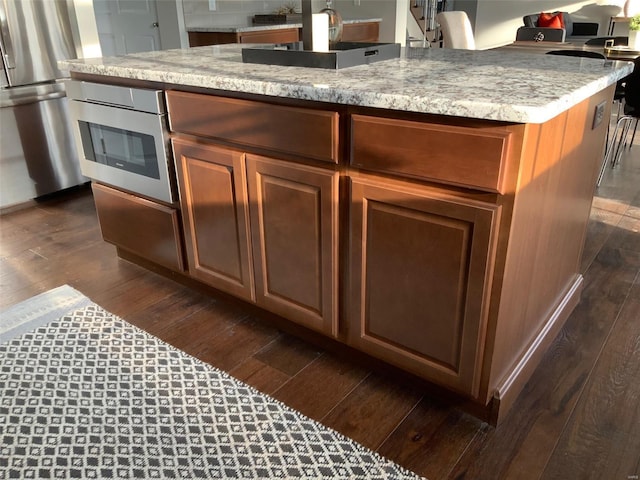 kitchen with light stone countertops, appliances with stainless steel finishes, a kitchen island with sink, sink, and dark hardwood / wood-style floors