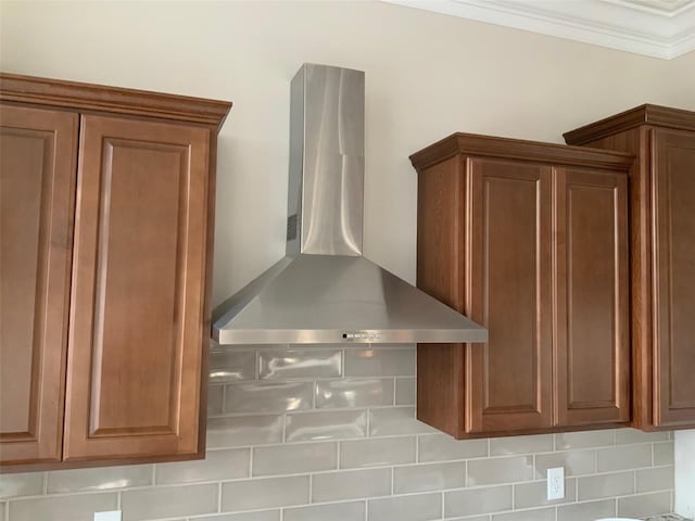 details featuring wall chimney exhaust hood, crown molding, and tasteful backsplash