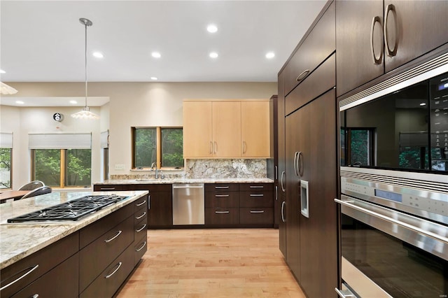 kitchen with pendant lighting, light hardwood / wood-style flooring, light stone countertops, tasteful backsplash, and stainless steel appliances