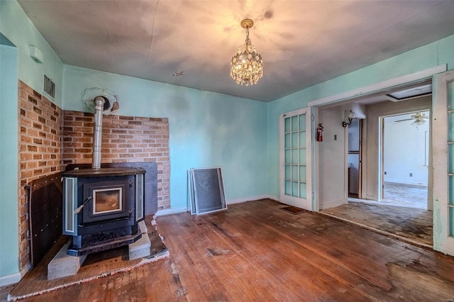 unfurnished living room with hardwood / wood-style flooring, visible vents, a ceiling fan, baseboards, and a wood stove