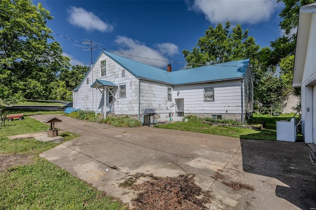 rear view of house with metal roof, a chimney, and a lawn