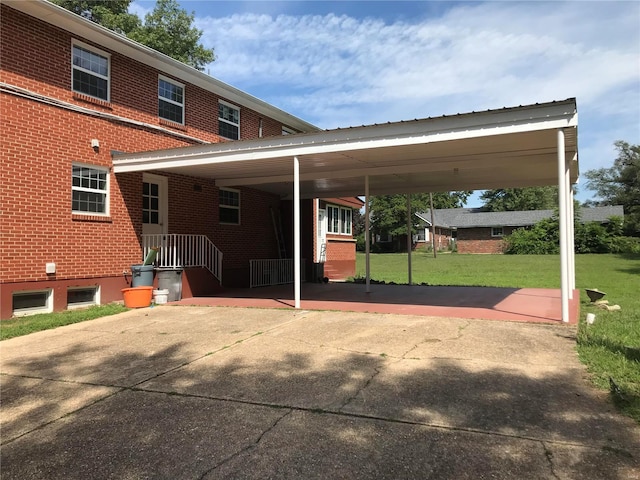 exterior space featuring an attached carport, brick siding, driveway, and a lawn