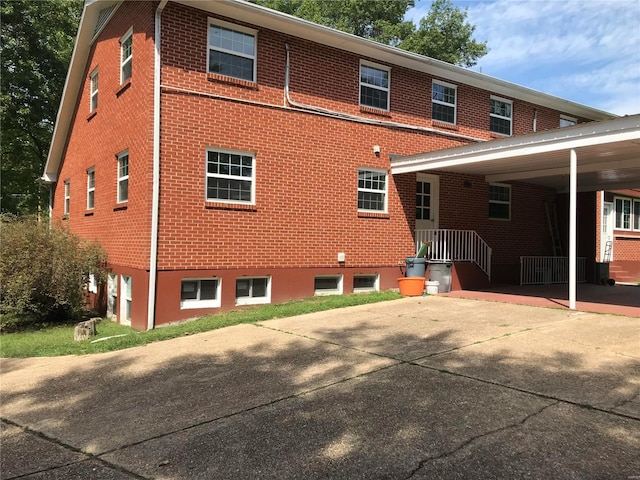 back of house featuring driveway, a carport, and brick siding