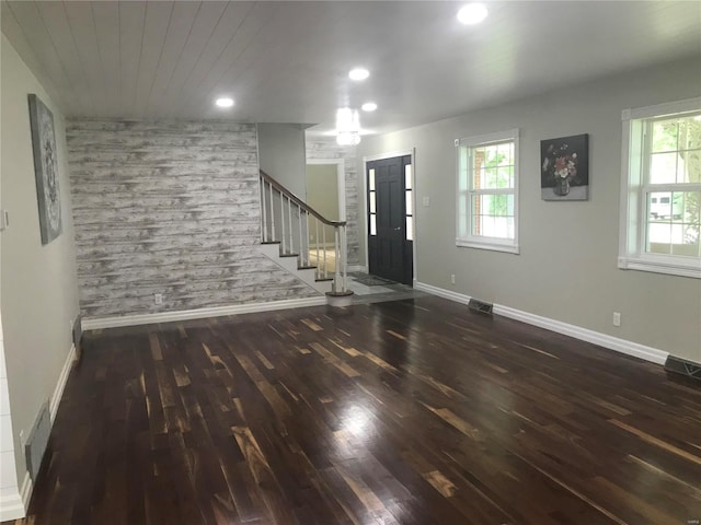 foyer entrance with a healthy amount of sunlight, stairs, an accent wall, and dark wood-style flooring