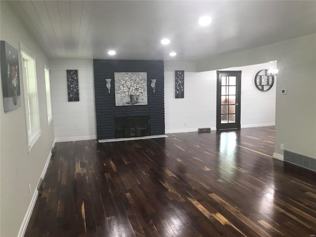 unfurnished living room featuring baseboards, visible vents, dark wood-style flooring, a brick fireplace, and recessed lighting