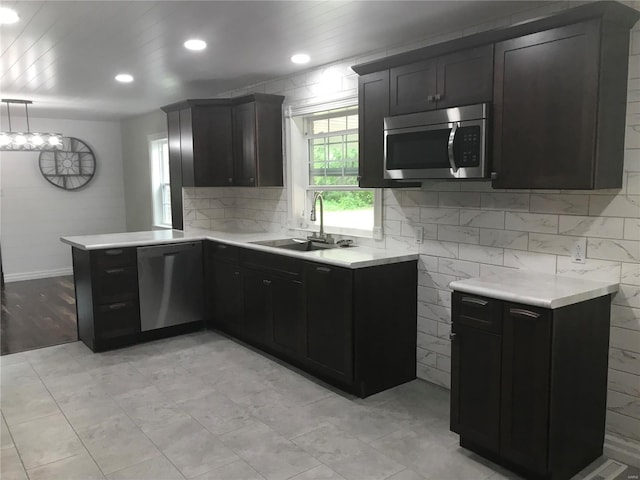 kitchen featuring tasteful backsplash, appliances with stainless steel finishes, a peninsula, light countertops, and a sink