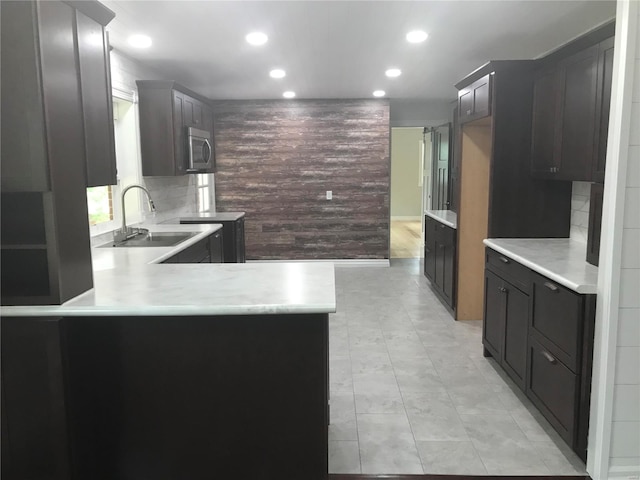 kitchen with stainless steel microwave, a peninsula, a sink, light countertops, and backsplash