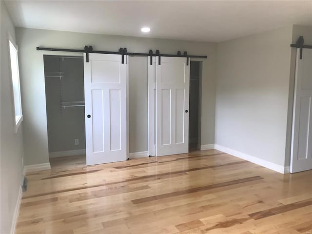 unfurnished bedroom featuring a barn door, baseboards, light wood-style flooring, and recessed lighting