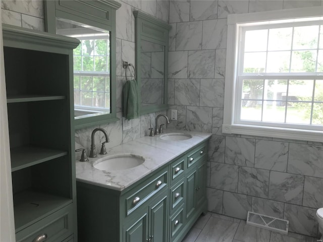 bathroom with visible vents, a sink, tile walls, and double vanity