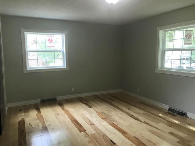 empty room featuring light wood finished floors, visible vents, and baseboards