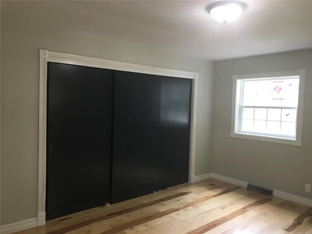 unfurnished bedroom featuring light wood finished floors, a closet, visible vents, and baseboards