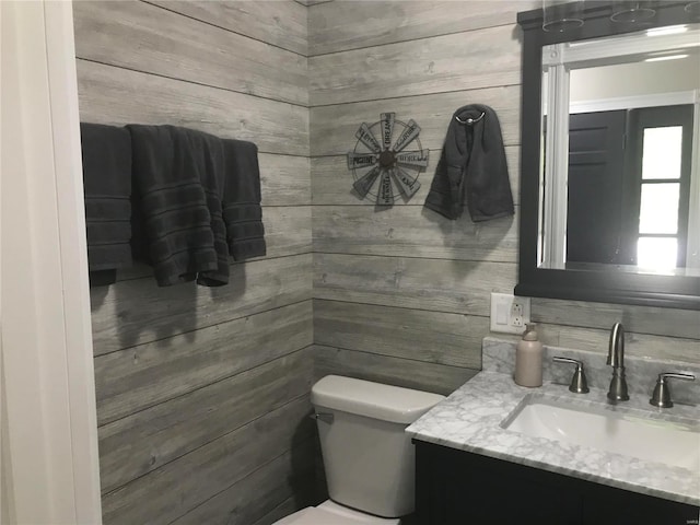 half bathroom featuring toilet, wooden walls, and vanity