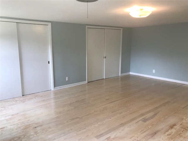 unfurnished bedroom featuring light wood-style floors, baseboards, and two closets