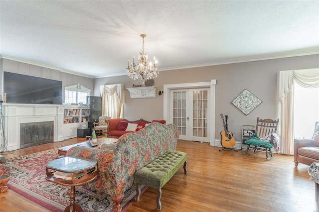 living room with french doors, ornamental molding, a textured ceiling, a notable chandelier, and light hardwood / wood-style floors