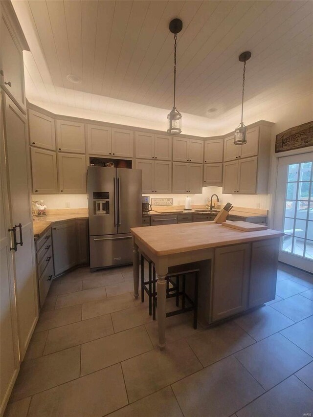 kitchen with hanging light fixtures, sink, stainless steel fridge, and tile flooring