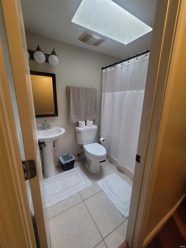 bathroom featuring tile flooring, a skylight, and toilet