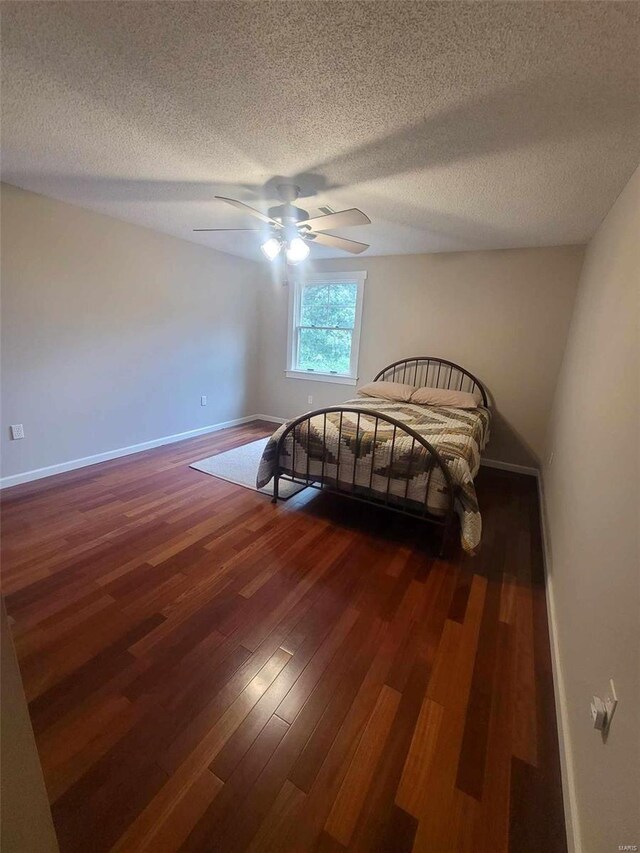 bedroom with ceiling fan, a textured ceiling, and dark wood-type flooring