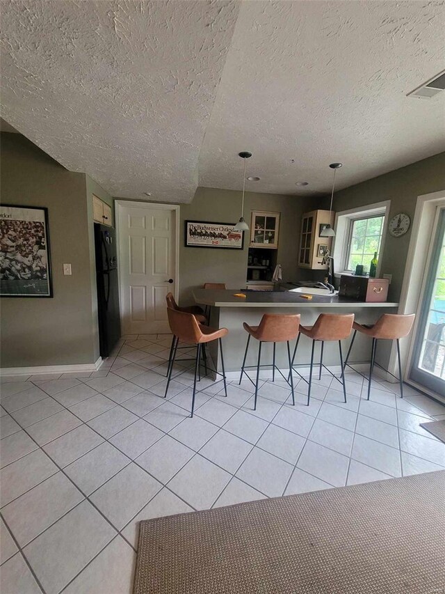 kitchen featuring a kitchen breakfast bar, kitchen peninsula, pendant lighting, black refrigerator, and a textured ceiling