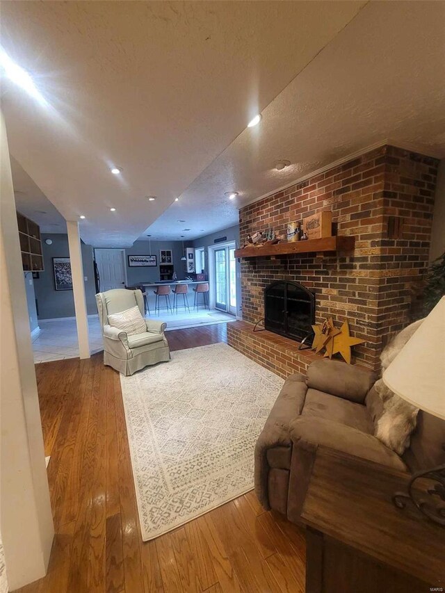 living room with a textured ceiling, hardwood / wood-style flooring, brick wall, and a brick fireplace