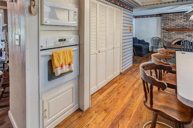 kitchen featuring brick wall, white appliances, light wood-type flooring, and a fireplace