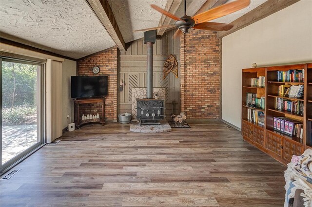 unfurnished living room featuring a textured ceiling, lofted ceiling with beams, a wood stove, and hardwood / wood-style floors