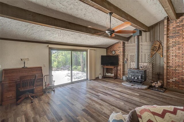 unfurnished living room with a textured ceiling, vaulted ceiling with beams, hardwood / wood-style floors, a wood stove, and ceiling fan