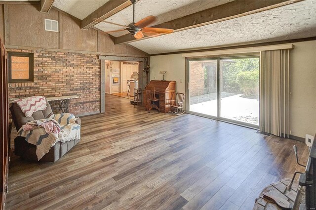 living area with ceiling fan, lofted ceiling with beams, hardwood / wood-style flooring, and a textured ceiling