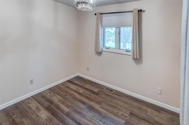 spare room with a chandelier and dark wood-type flooring