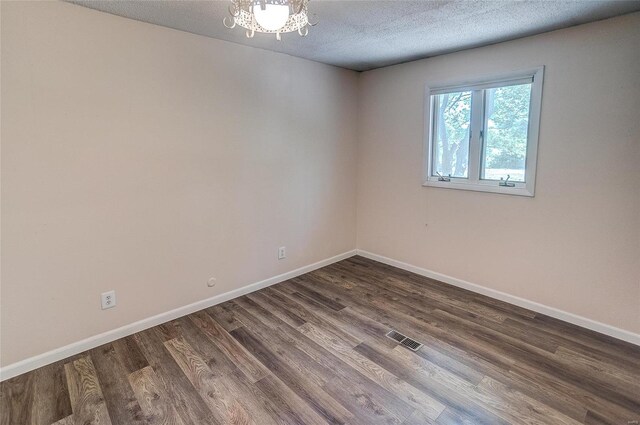 empty room featuring a textured ceiling, dark wood-type flooring, and an inviting chandelier