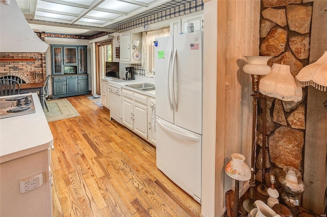 kitchen with white cabinetry, light wood-type flooring, custom range hood, white appliances, and a brick fireplace