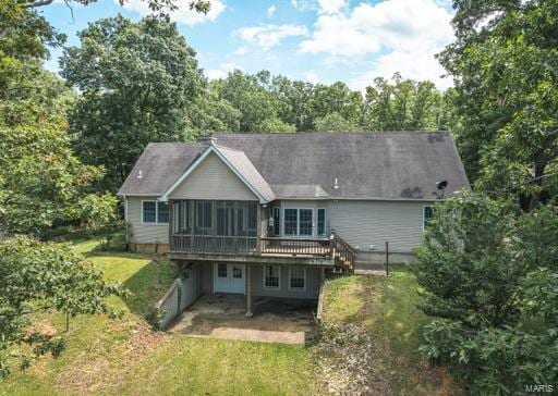 rear view of property featuring a wooden deck, a sunroom, a patio, and a lawn