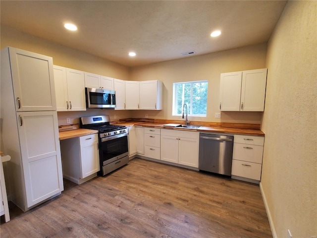 kitchen with stainless steel appliances, sink, hardwood / wood-style flooring, and butcher block counters