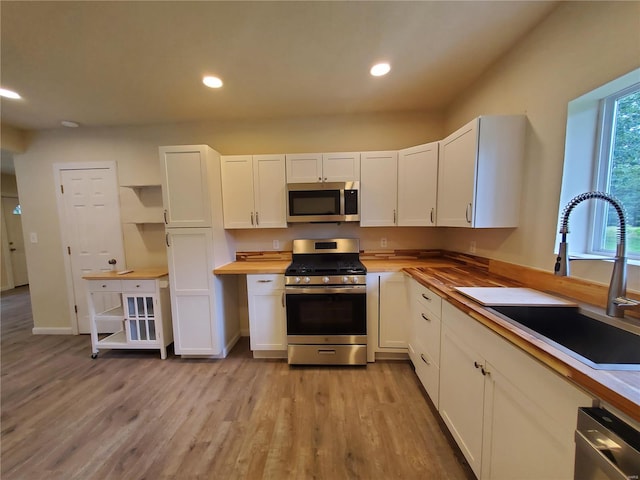 kitchen featuring light hardwood / wood-style floors, butcher block counters, sink, white cabinets, and appliances with stainless steel finishes