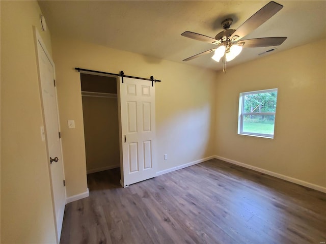 unfurnished bedroom featuring a barn door, ceiling fan, a closet, and hardwood / wood-style flooring