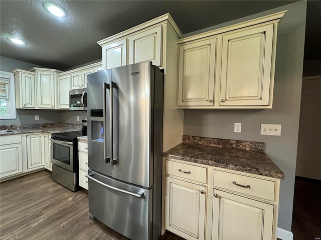 kitchen with stainless steel appliances, dark hardwood / wood-style floors, a textured ceiling, and cream cabinetry