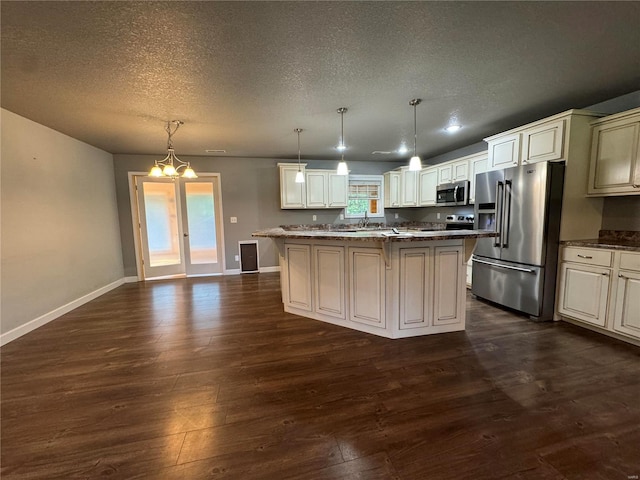 kitchen featuring appliances with stainless steel finishes, an inviting chandelier, hanging light fixtures, dark hardwood / wood-style floors, and a kitchen island