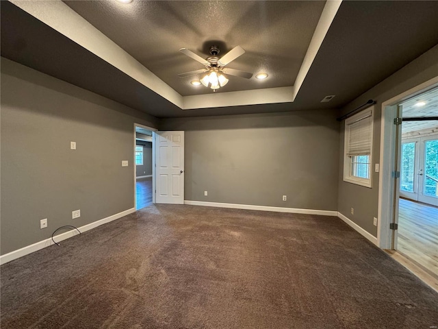 carpeted spare room with a raised ceiling and ceiling fan