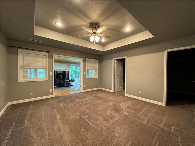 unfurnished living room with ceiling fan, a tray ceiling, a textured ceiling, and dark colored carpet