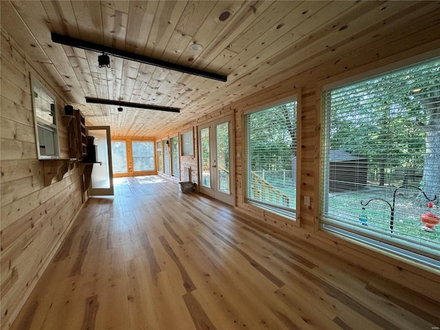 unfurnished living room featuring rail lighting, wooden walls, wood ceiling, and light hardwood / wood-style flooring