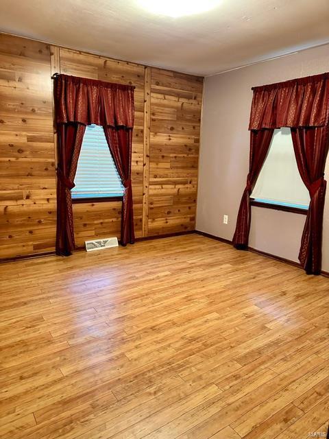 unfurnished room with light wood-type flooring and wood walls