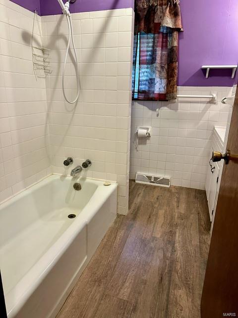 bathroom featuring hardwood / wood-style floors, tiled shower / bath combo, and tile walls